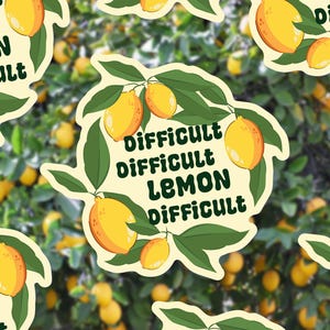 Puede incluir: Una pegatina con un diseño de rama de limón, que muestra limones amarillos y hojas verdes. El texto "Difficult Lemon Difficult" está en verde oscuro. El fondo es una imagen borrosa de un limonero.