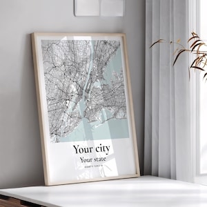 May include: A framed vertical wall art print featuring a black and white street map of a city over a light blue background. The text "Your city" and "Your state" is printed in black below the map, followed by a line of smaller coordinates.