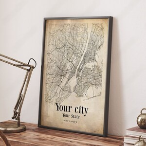 May include: A black framed print of a vintage style map of a city with the text "Your city" and "Your State" below the map.