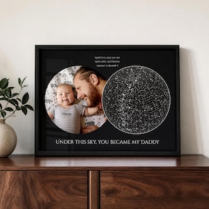 May include: A black framed wall art print featuring a circular photograph of a baby held by an adult, next to a circular star map. Text reads: MARCH 9, 2023 3:16 AM ADELAIDE, AUSTRALIA -34.9244° S 138.5998° E and UNDER THIS SKY, YOU BECAME MY DADDY.