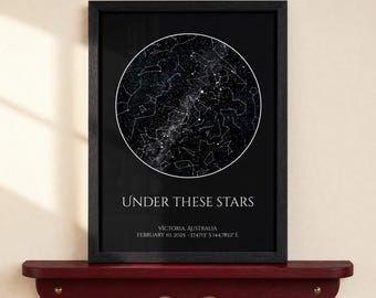 May include: A black framed wall art print featuring a circular star map on a black background. The text reads UNDER THESE STARS, VICTORIA, AUSTRALIA, FEBRUARY 10, 2025 -37.4713° S 144.7852° E in white capital letters below the star chart.