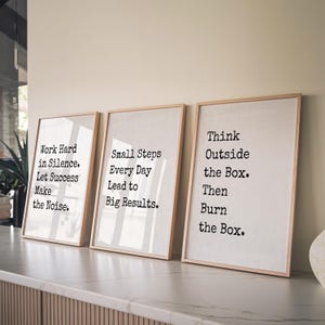 Pu&ograve; includere: Tre stampe artistiche verticali incorniciate con cornici in legno chiaro. Ogni stampa presenta testo nero in stile macchina da scrivere su sfondo bianco. Il testo recita: Work Hard in Silence. Let Success Make the Noise. Small Steps Every Day Lead to Big Results. Think Outside the Box. Then Burn the Box.