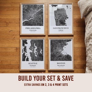 May include: Four framed wall art prints featuring black and white map designs of Philadelphia, San Francisco, Seattle, and Boston. Each print includes the city name, state, and coordinates in a clean, sans-serif font within a light wood frame.