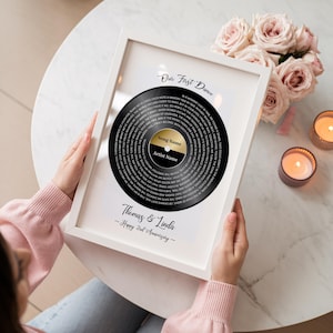 May include: A framed black vinyl record art print with the text "Our First Dance." The record has a gold center with space for a song and artist name. The frame includes the names "Thomas & Linda" and "Happy 2nd Anniversary."