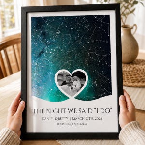 Könnte beinhalten: Ein gerahmter Kunstdruck mit einem dunkelblauen und türkisfarbenen Nachthimmel mit weißen Sternbildern. Ein herzförmiges Schwarz-Weiß-Foto eines Paares ist zentriert. Der Text lautet: THE NIGHT WE SAID "I DO" DANIEL & BETTY | MARCH 27TH, 2024 BRISBANE QLD, AUSTRALIA.