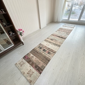 May include: A long, narrow, beige and brown runner rug with a geometric pattern. The rug has a faded, vintage look and is made of wool.