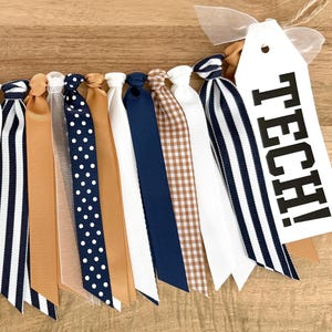 May include: A decorative banner with various ribbons in white, navy, tan, and brown. Some ribbons have polka dots, stripes, or a gingham pattern. A white tag with the word "TECH!" in black is attached.