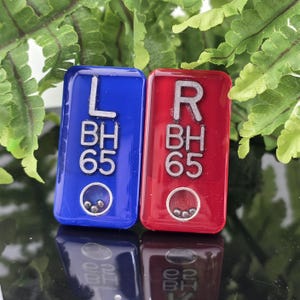May include: Two rectangular resin markers, one blue and one red, each featuring the silver embossed text L BH 65 or R BH 65. Each marker includes a small circular window at the bottom containing three tiny metallic ball bearings that move freely.