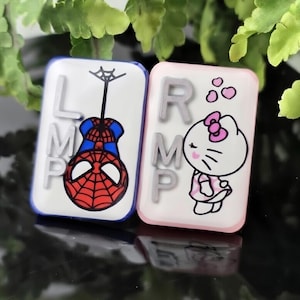 May include: Two rectangular magnets. One features a Spider-Man design with the letters L, M, and P. The other has a Hello Kitty design with the letters R, M, and P. Both have a glossy finish. Measurements are in centimetres.