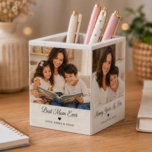 May include: A white square desk organizer featuring custom photo prints of a woman and two children reading a book. The front displays the text Best Mom Ever, LOVE, EMMA & NOAH, and the side shows Mommy, You're My Hero, LOVE ALWAYS, NOAH.
