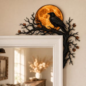 May include: A black raven perched on a dark, gnarled tree branch that extends along the corner of a white door frame. Behind the bird is a circular, glowing orange moon. Small, rust-colored autumn leaves are attached to the black tree branches.