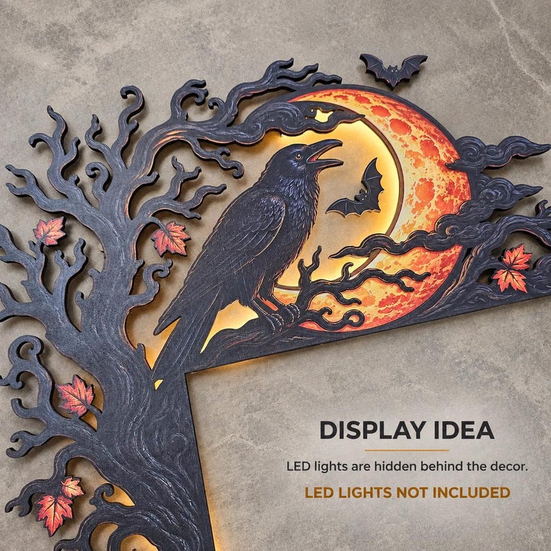 May include: A black wooden wall decoration featuring a large raven perched on a tree branch against a glowing orange moon. The design includes swirling tree branches, small bats, and orange autumn leaves. Text reads: DISPLAY IDEA LED lights are hidden behind the decor. LED LIGHTS NOT INCLUDED.