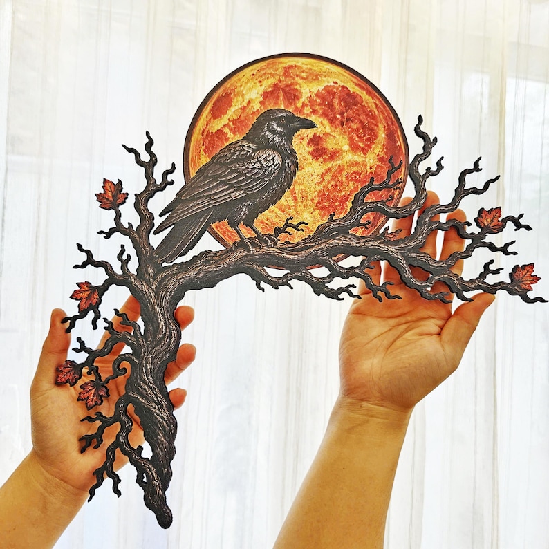 May include: A flat decorative wall hanging featuring a black raven perched on a dark, gnarled tree branch. Behind the bird is a large, textured orange and red full moon. The branch is adorned with small, detailed autumn leaves in shades of red.