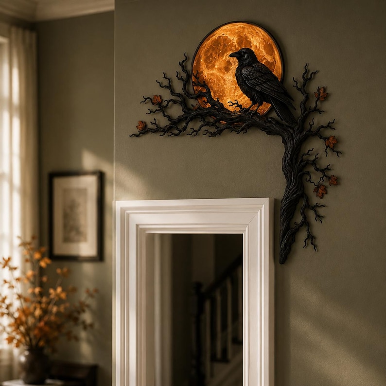 May include: A wall-mounted decorative piece featuring a black raven perched on a dark, gnarled tree branch. Behind the bird is a circular, glowing orange moon with a textured surface. Small, scattered orange leaves accent the dark, twisted branches.
