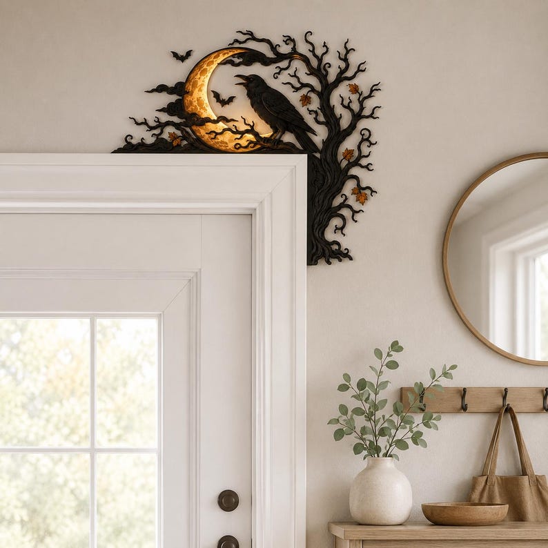 May include: A black decorative door corner accent featuring a silhouette of a tree with a glowing crescent moon and a perched raven. The design includes small bats and scattered orange leaves, crafted to fit the upper corner of a door frame.