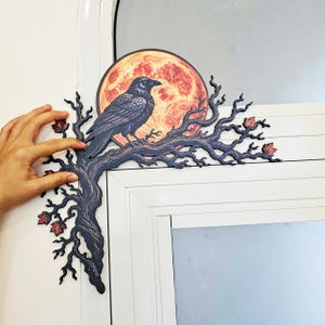 May include: A decorative corner wall accent featuring a black raven perched on a dark, gnarled tree branch. Behind the bird is a large, circular, textured orange and red full moon. Small, dark red autumn leaves are scattered along the branches.