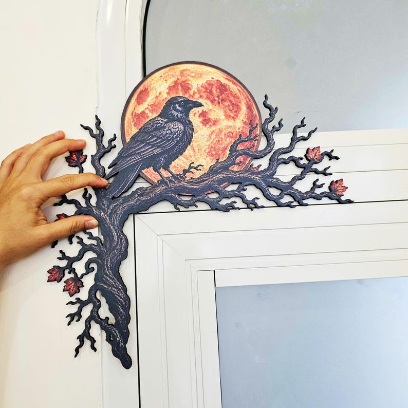 May include: A decorative corner wall accent featuring a black raven perched on a dark, gnarled tree branch. Behind the bird is a large, circular, textured orange and red full moon. Small, dark red autumn leaves are scattered along the branches.