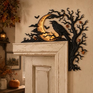 May include: A black wall decoration featuring a crescent moon with a textured surface, a perched raven, and bare tree branches. Small bats are positioned near the moon, and orange autumn leaves are scattered among the dark, twisted tree limbs.