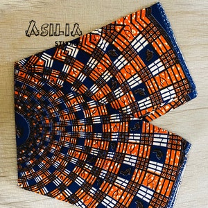May include: A close-up of a fabric with a geometric pattern in orange, white, and blue. The fabric has a circular design with a repeating pattern of squares and lines.
