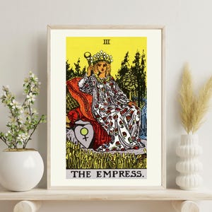 Op de afbeelding: Een ingelijste tarotkaart print van "The Empress". De afbeelding toont een vrouw in een witte jurk met rode bloemaccenten, zittend op een troon. De achtergrond is geel met een boslandschap. De kaart is gelabeld met "III" en "THE EMPRESS."