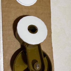 May include: A close-up of a gold-colored caster wheel with a white plastic ring around the center. The wheel has three spokes and a small screw in the center. There are two white plastic rings, one on top of the other, above the wheel.