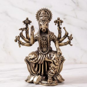 May include: Bronze-colored statue of a deity with a pig's head and multiple arms, seated on a lotus flower base. The statue is adorned with intricate jewelry and a halo, showcasing detailed craftsmanship and religious symbolism.