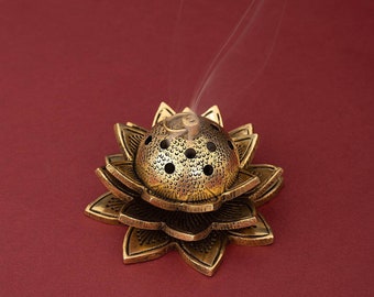 May include: A gold metal incense burner shaped like a lotus flower with smoke rising from the top. The burner has a round, perforated top and three layers of petals.