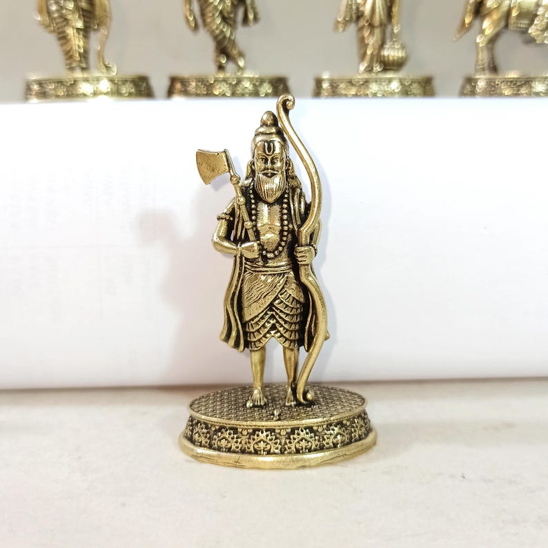 May include: A gold-colored metal figurine of a Hindu deity holding an axe and bow. The figurine is standing on a decorative base.