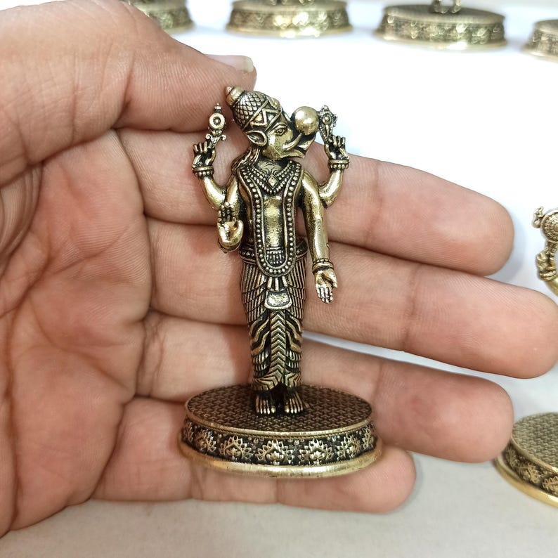 May include: A gold-colored metal figurine of a Hindu deity with four arms, holding various objects. The figurine is standing on a round base with intricate designs.