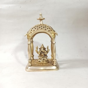 May include: A gold-colored metal statue of Ganesha, the Hindu god of wisdom and prosperity, is placed inside a decorative, ornate, gold-colored metal temple structure.