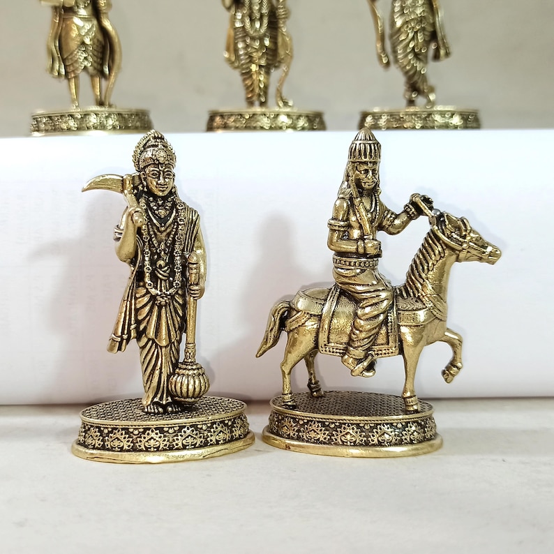 May include: Two gold-colored figurines of Hindu deities. One figurine depicts a deity standing with a staff and a mace. The other figurine depicts a deity riding a horse.