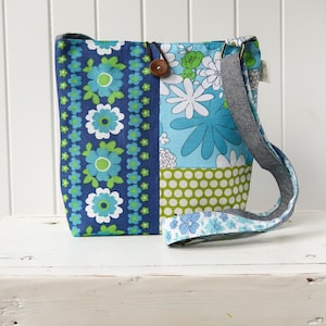 May include: A blue and green patchwork fabric shoulder bag with a floral print. The bag has a long adjustable strap.