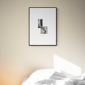 May include: A black framed picture with a white background and two black and white photographs of hands. The picture is hanging on a beige wall above a white bed with a white duvet and pillows.