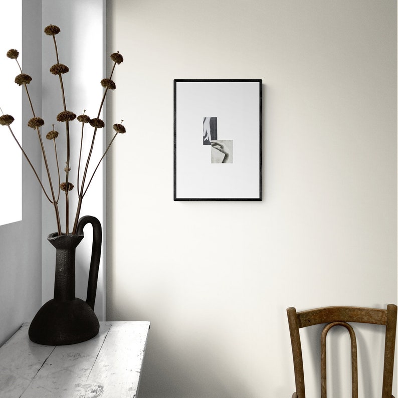 May include: A black and white framed photo collage with two images of a person's hand and arm. The photo is hanging on a white wall above a white wooden table and a wooden chair.