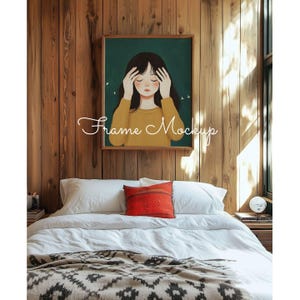 May include: A framed illustration of a girl with her eyes closed, wearing a yellow sweater against a green background. The frame is on a wooden wall above a white bed with a red and white throw pillow and a brown and white blanket.