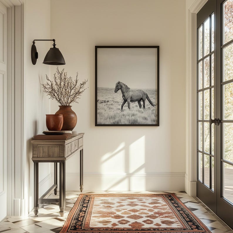 May include: A rustic wooden console table with a brown and black rug underneath. A black and white photograph of a horse running in a field hangs on the wall above the table. A vase with dried branches sits on the table.
