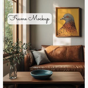 May include: A framed print of a brown and gray bird with a yellow background hanging on a wall above a brown leather couch. The couch has a gray pillow and is in a room with a window and a wooden coffee table.