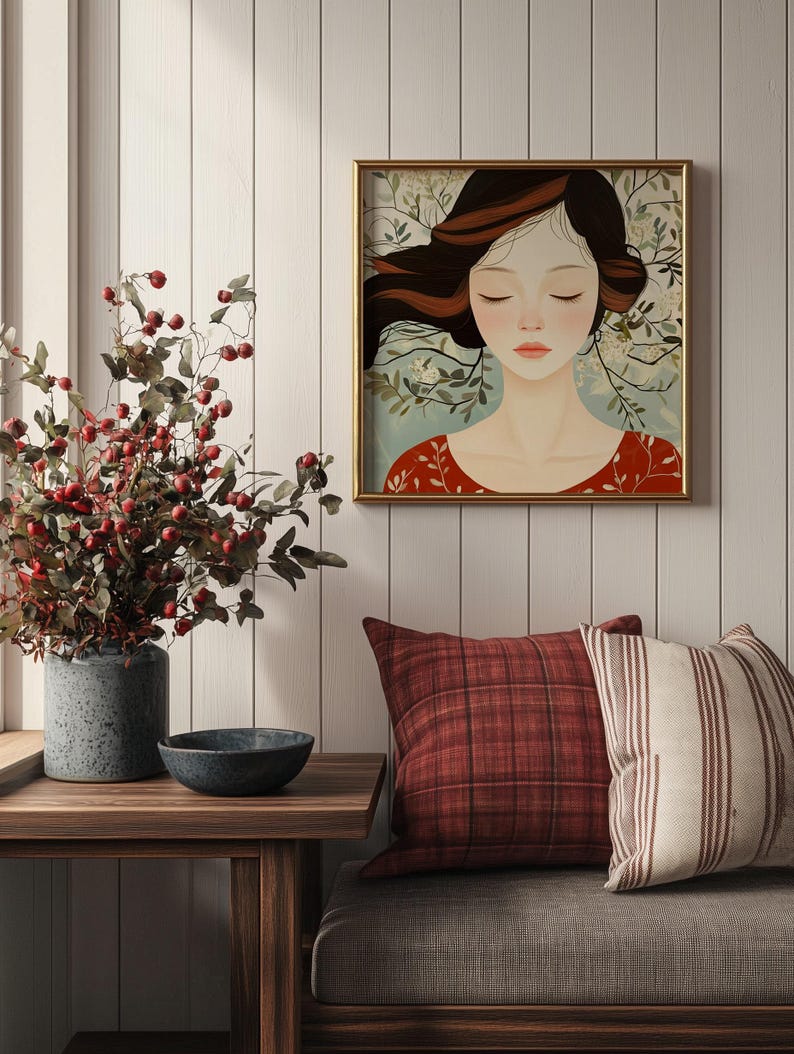 May include: A framed illustration of a woman with long brown hair, closed eyes, and a red dress. The woman is surrounded by white flowers and green leaves. The frame is gold and the background is a white wood panel.