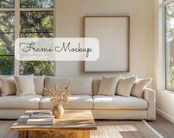 May include: A white sofa with cushions sits in a living room with a large window and a wooden coffee table. A framed picture hangs on the wall above the sofa. The text "Frame Mockup" is written on a white rectangle in the image.