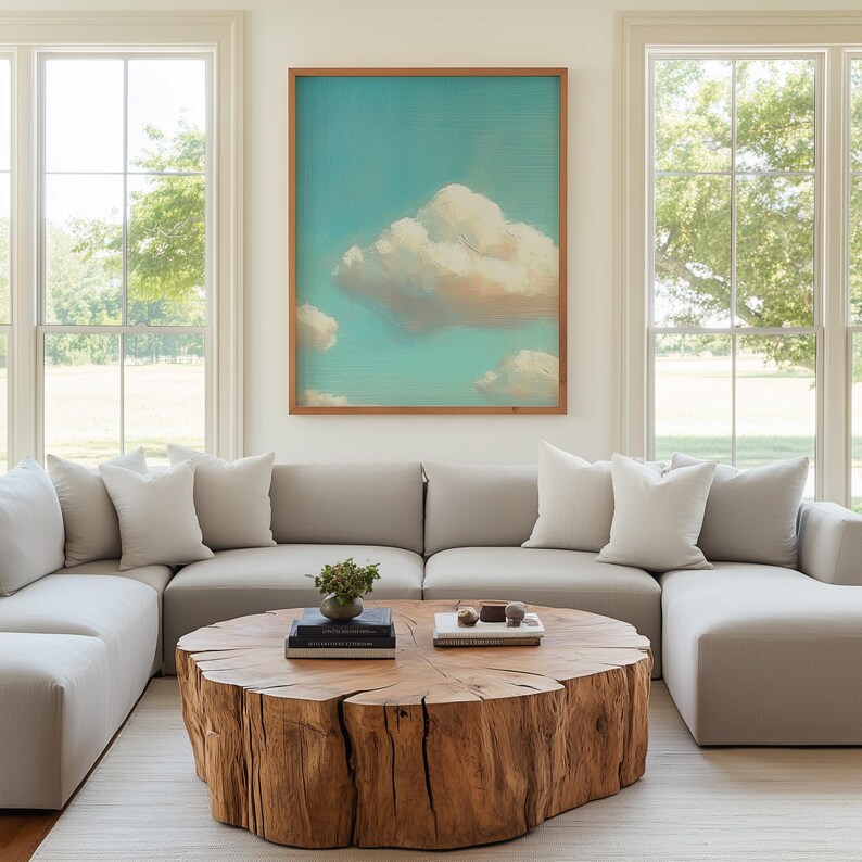 May include: A living room with a large, light gray sectional sofa, white pillows, and a round wooden coffee table. A framed artwork of clouds hangs on the wall. Large windows offer a view of the outdoors.