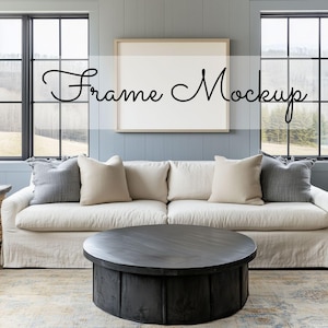 May include: A living room scene featuring a white sofa with gray and beige pillows, a dark round coffee table, and a framed artwork on a blue wall. The text "Frame Mockup" is displayed on the artwork.
