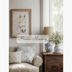 Op de afbeelding: Een tekening van een wit paardenhoofd in een houten lijst hangt aan een muur boven een beige bank met blauw-witte gepatroneerde kussens. Een lamp met een beige kap staat op een houten bijzettafel met twee blauw-witte keramische vazen.