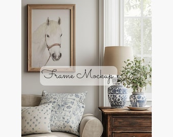 May include: A white horse head drawing in a wooden frame hangs on a wall above a beige couch with blue and white patterned pillows. A lamp with a beige shade sits on a wooden side table with two blue and white ceramic vases.