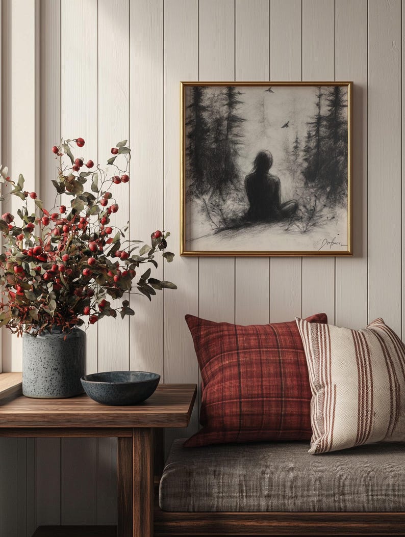 May include: A gray couch with red and white patterned throw pillows. A framed black and white drawing of a person sitting in a forest hangs on the wall above the couch. A vase with red berries and green leaves sits on a wooden table in front of the couch.