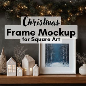 May include: A square art frame mockup with the text "Christmas Frame Mockup for Square Art." The frame displays a winter landscape painting. Decorative ceramic houses and a small Christmas tree are arranged on a wooden shelf, with a garland of lights above.