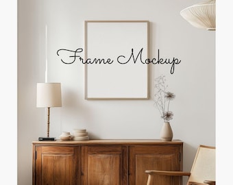 May include: A wooden cabinet with three doors and a light brown finish. A white lamp with a cream shade sits on top of the cabinet. A framed picture hangs on the wall above the cabinet. The text "Frame Mockup" is written in black cursive on the wall.