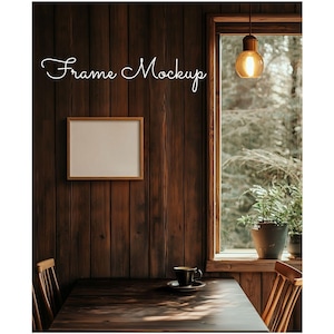 May include: A wooden framed picture mockup with a white background, hanging on a dark wood wall. A wooden table with a cup and saucer sits in front of the frame. A window with a view of trees and a hanging light fixture is in the background.