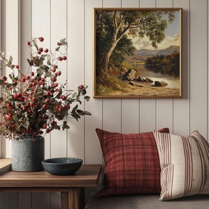 May include: A framed landscape painting of a lake with trees and mountains in the background. The painting is hanging on a white wall with a wooden bench and a vase of red berries in the foreground.
