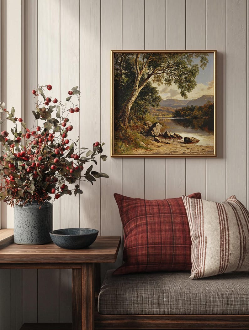 May include: A framed landscape painting of a lake with trees and mountains in the background. The painting is hanging on a white wall with a wooden bench and a vase of red berries in the foreground.