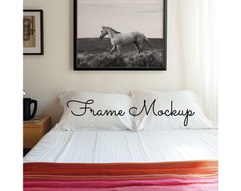 May include: A black and white photo of a horse running in a field is framed and hanging on a white wall above a white bed with a red and orange striped blanket.